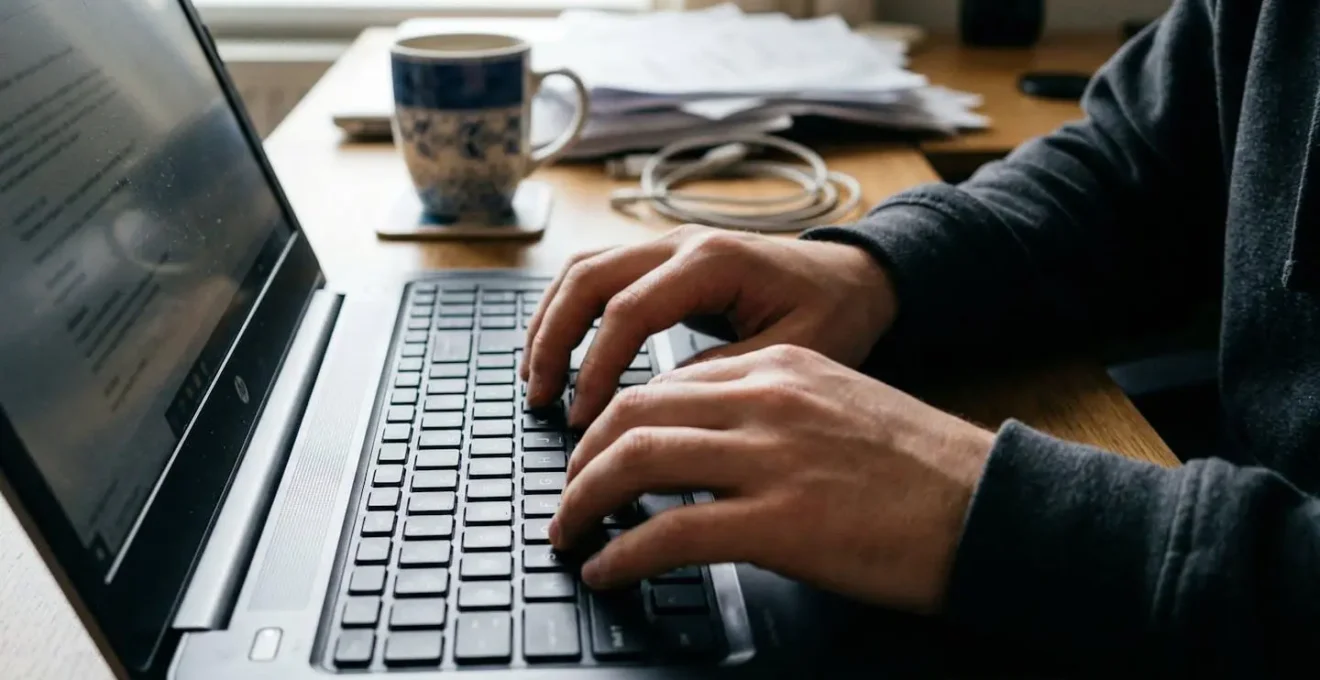 Gros plan sur des mains utilisant un clavier ordinateur portable avec écran flouté sur un bureau domestique éclairé naturellement